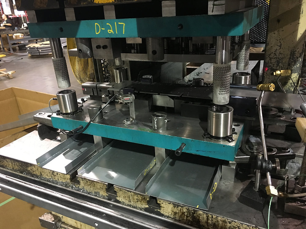 Close-up photograph of a progressive metal stamping die with formed sheet-metal parts and press tooling