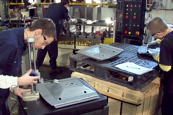 Progressive stamping die and formed metal parts undergoing dimensional inspection in a manufacturing quality-control area