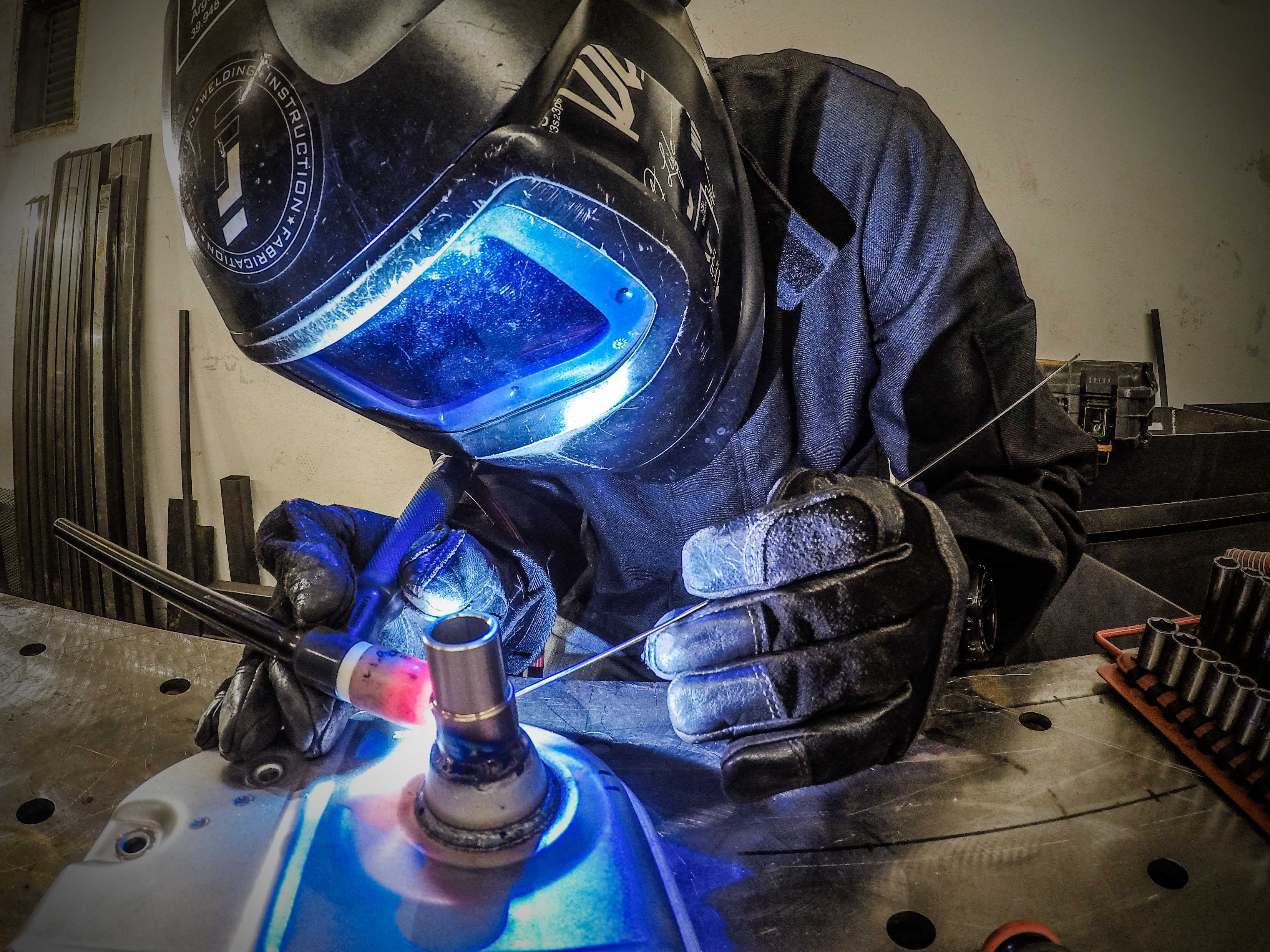 Welder wearing protective gloves and helmet performs TIG welding on a metal workpiece