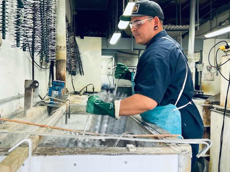 Worker in protective gloves handles metal parts at an active industrial finishing workstation