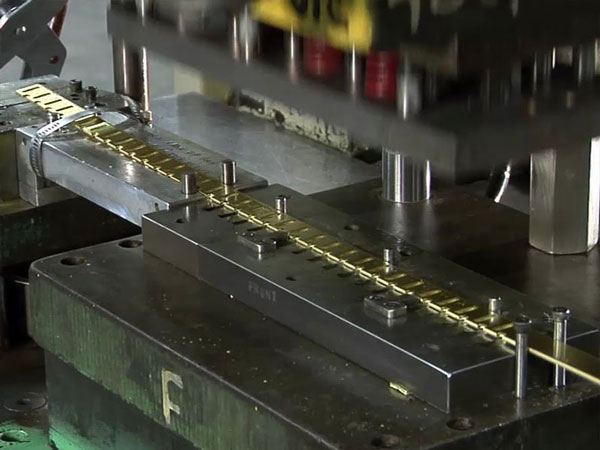 Close-up of a progressive stamping die forming metal strip inside an industrial press