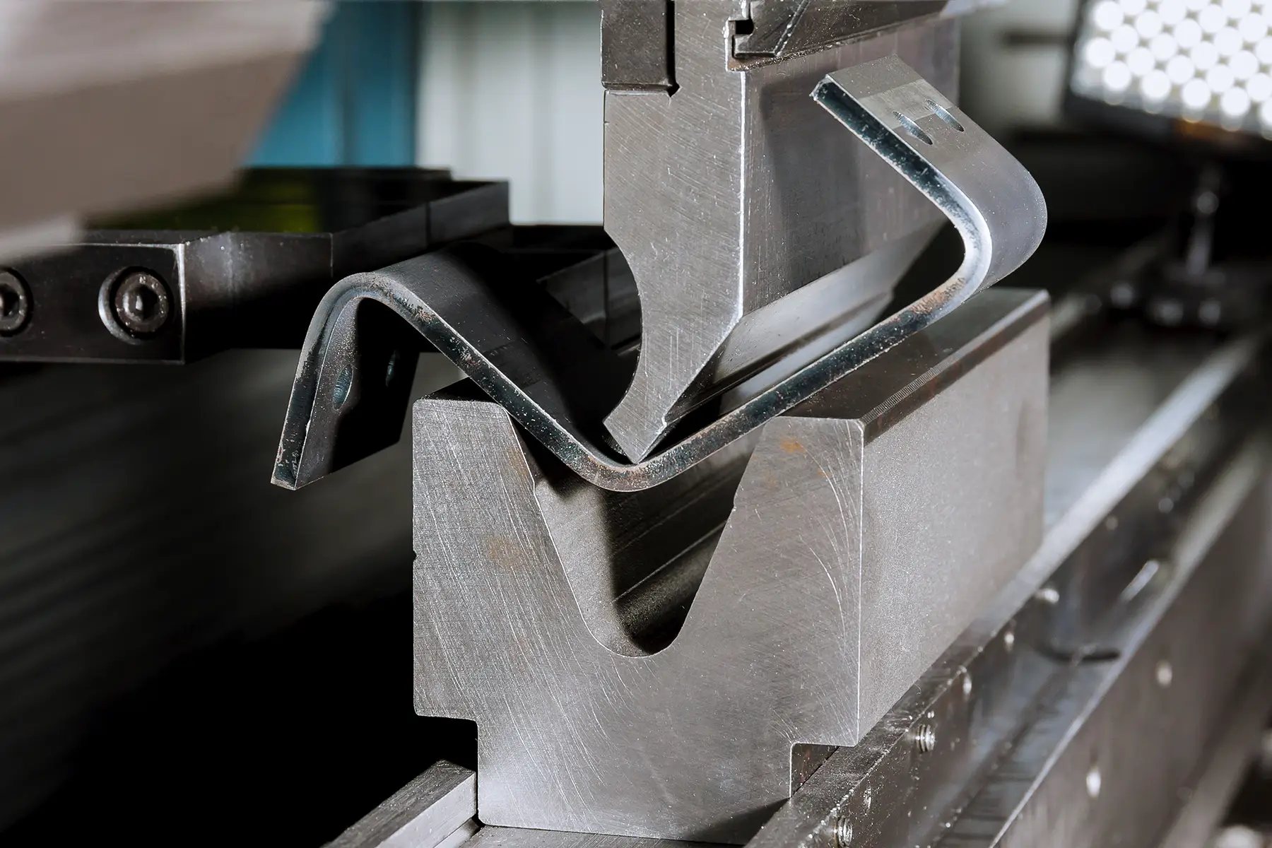 Close-up of a steel sheet being formed between press-brake tooling in a fabrication shop