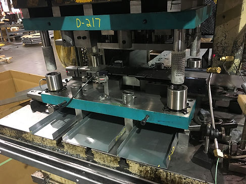 Close-up photograph of a progressive stamping die and metal strip inside an industrial press