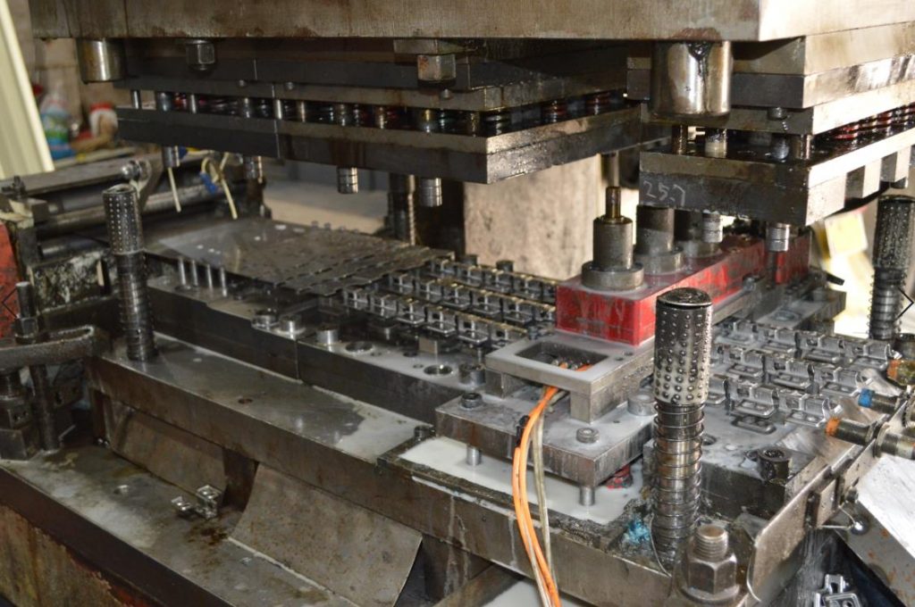 Progressive stamping die forming rows of metal hinge parts in a factory production line