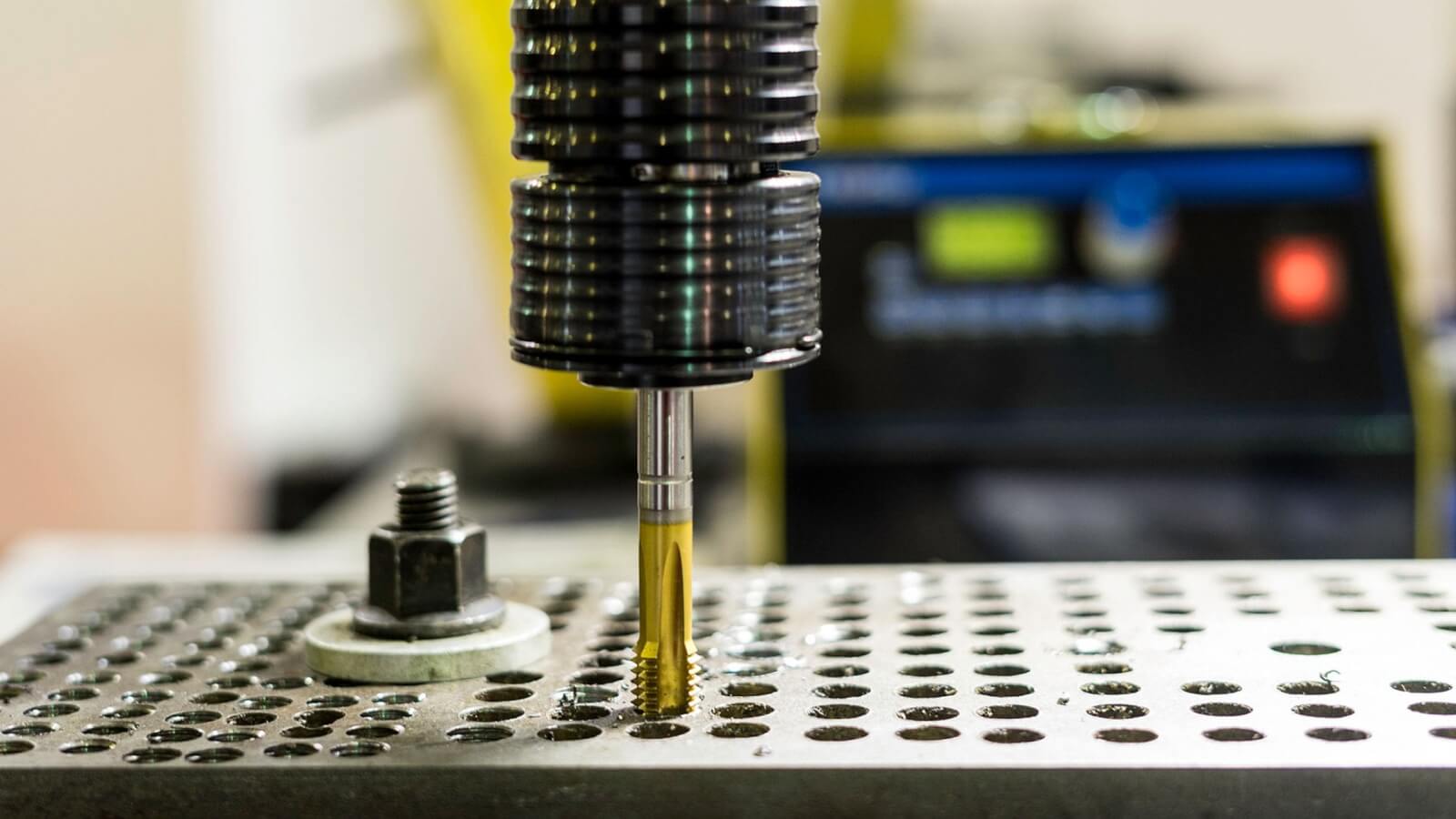 Machine tap cutting threads into a metal component at a machining station