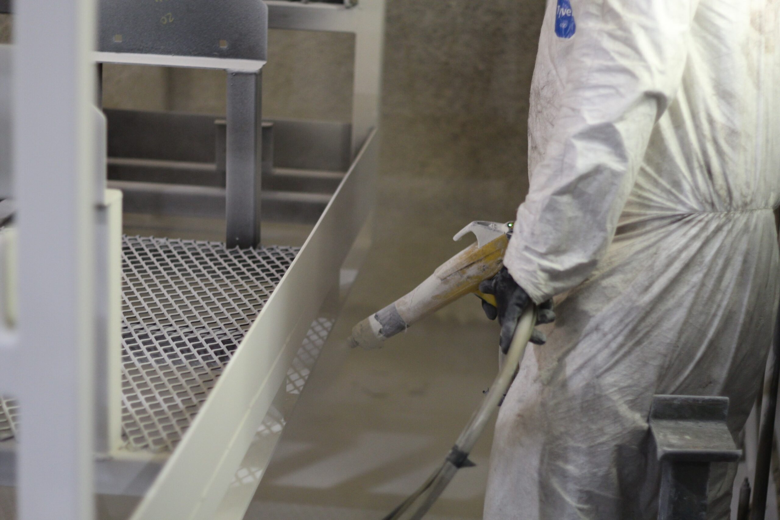 Technician applying white powder coating to custom metal parts inside an industrial finishing booth