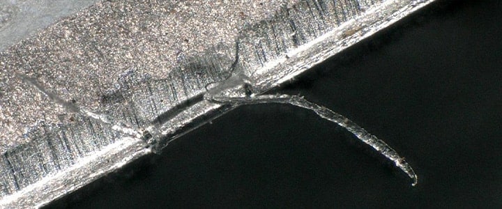 Microscopic close-up shows a sharp burr rising from the sheared edge of a pressed metal product