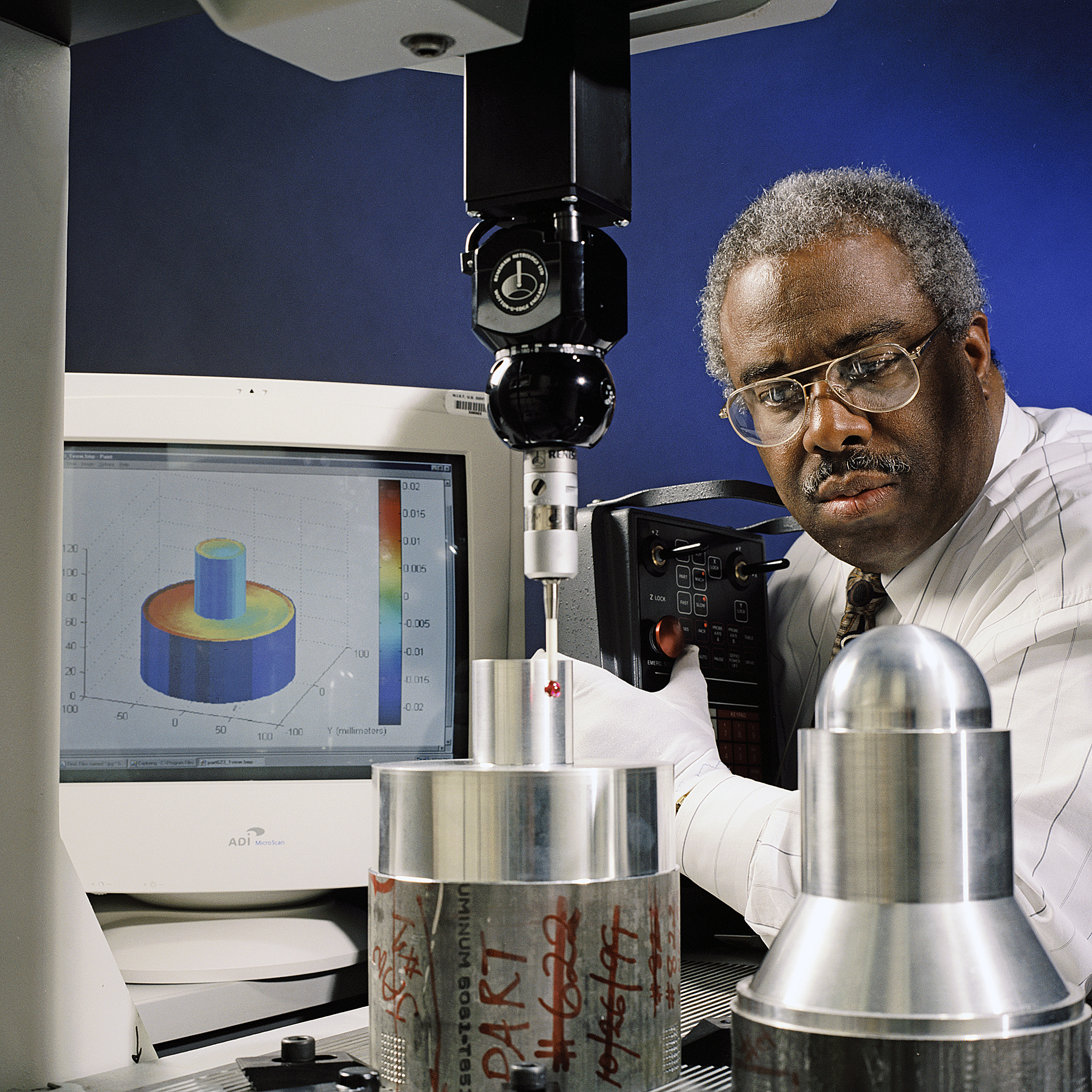 NIST engineer uses a coordinate measuring machine to inspect precision metal components beside dimensional analysis software