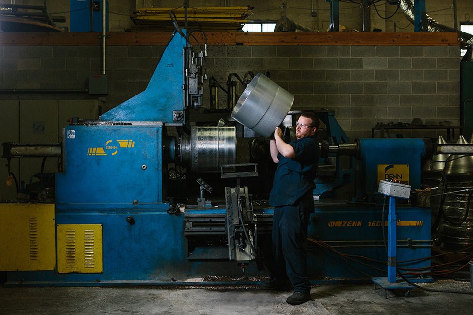 CNC spinning lathe forming a large circular metal blank against a mandrel