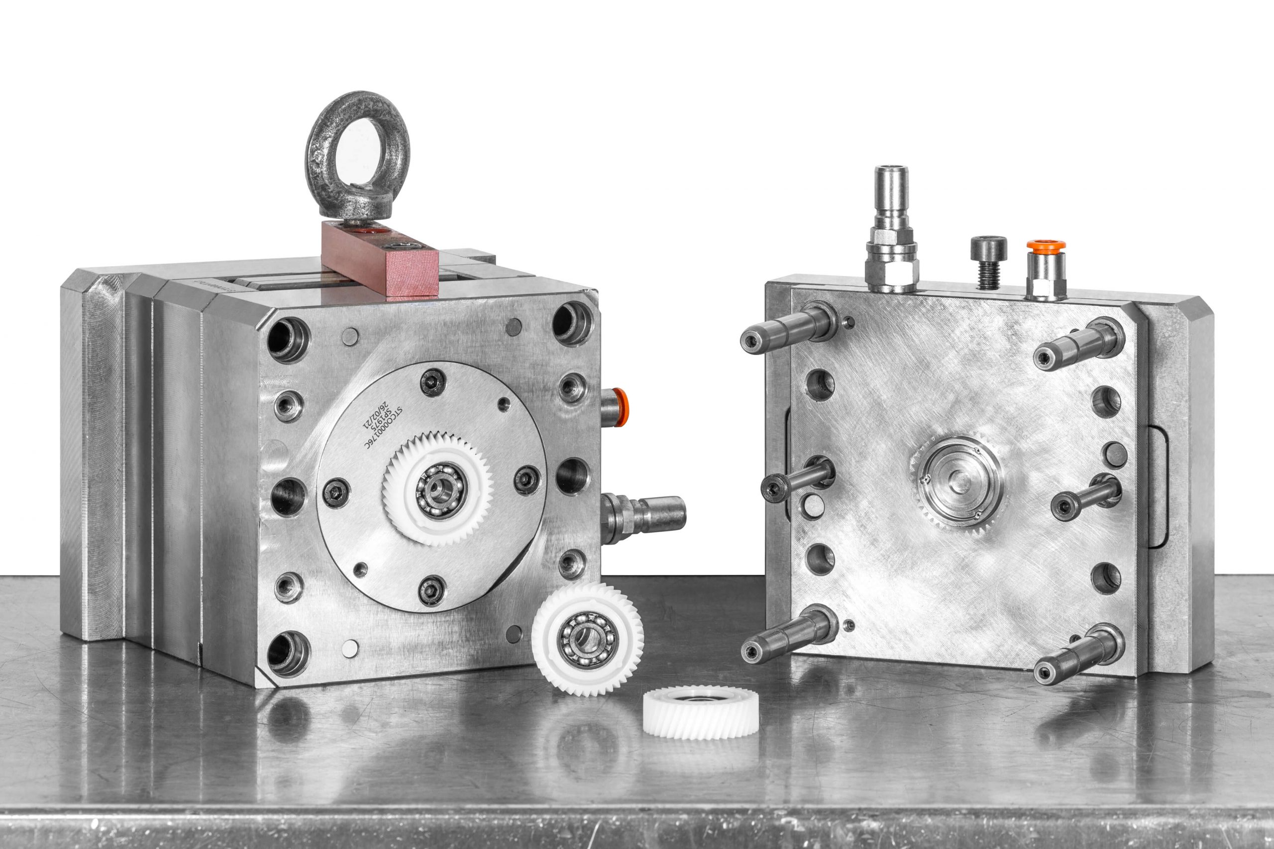 Open metal injection mold showing insert-molding tooling and a partially formed plastic gear component