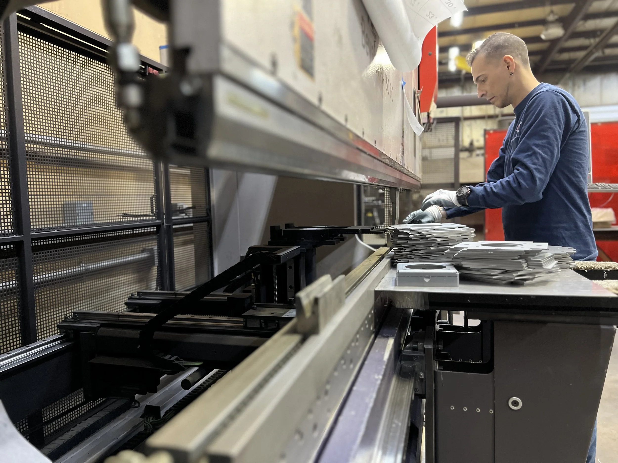 Fabrication worker operating a press brake while inspecting formed metal parts in a manufacturing shop