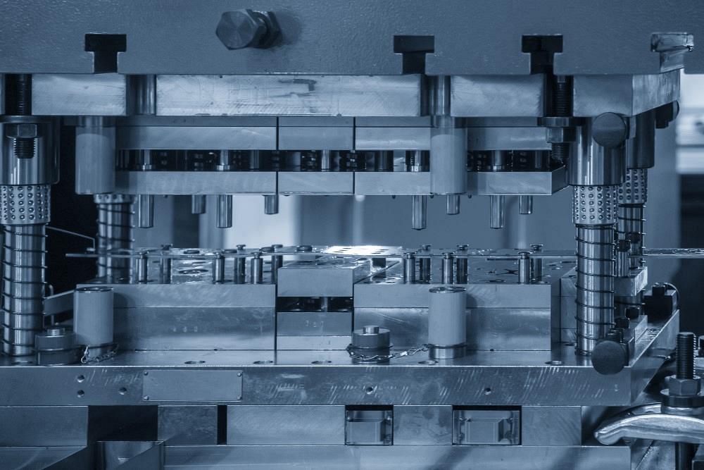 Close-up photograph of a progressive stamping die and metal carrier strip during industrial production